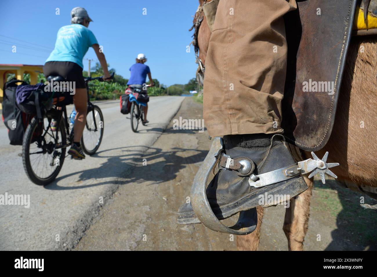 Cuba, eastern region, 2 cyclo tourists are passing in front a man riding a horse, only his leg and his spurs Stock Photo