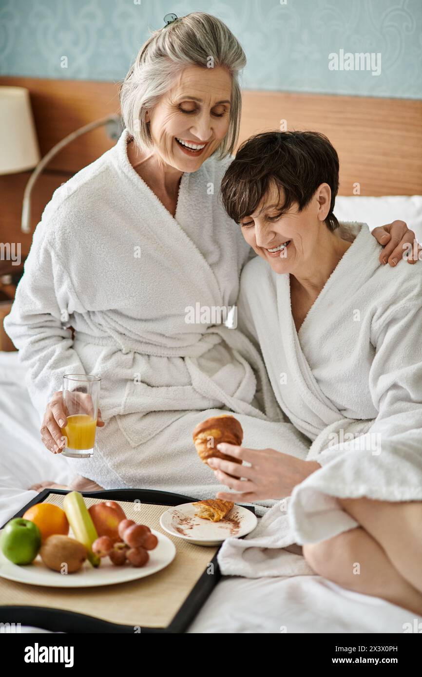 Senior lesbian couple shares a tender moment in a cozy bed at a hotel. Stock Photo