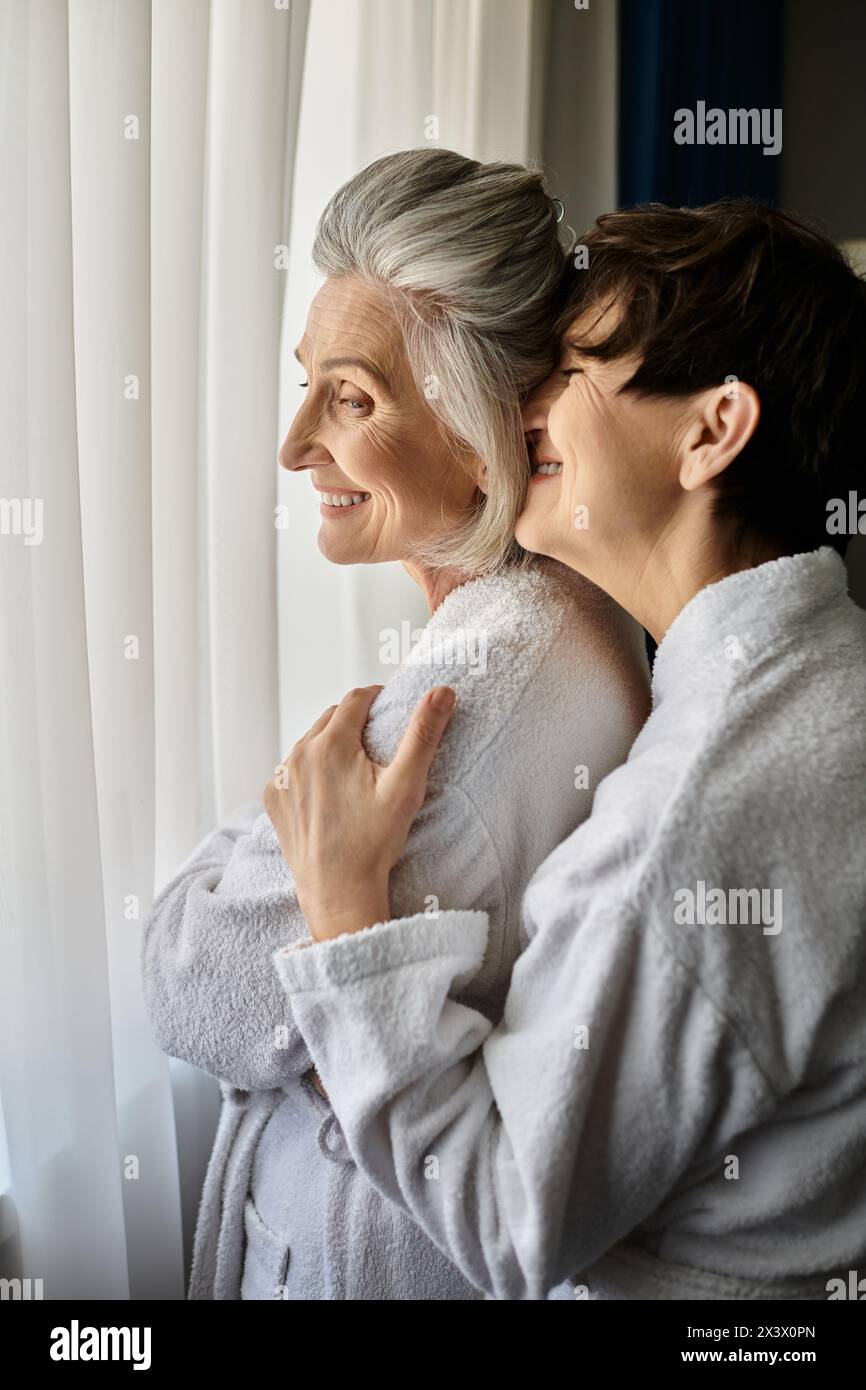Senior lesbian couple in a bathrobe peacefully enjoy the view together. Stock Photo