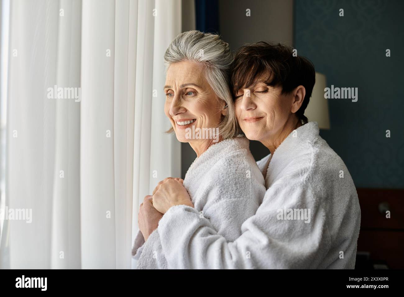 Senior lesbian couple embrace warmly in a hotel room. Stock Photo