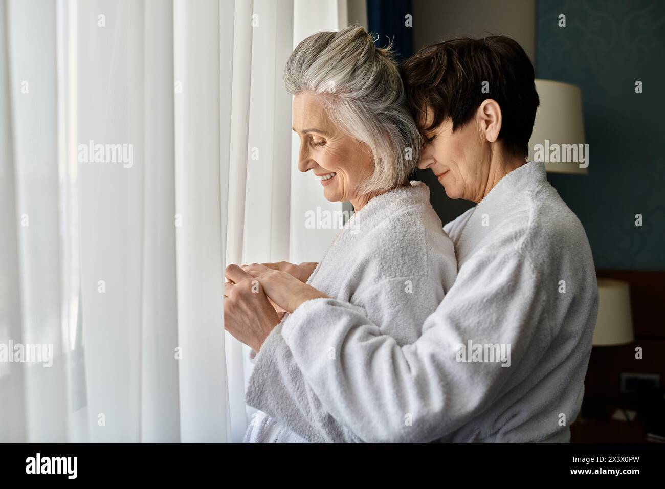 Senior lesbian couple share a quiet moment by the window. Stock Photo