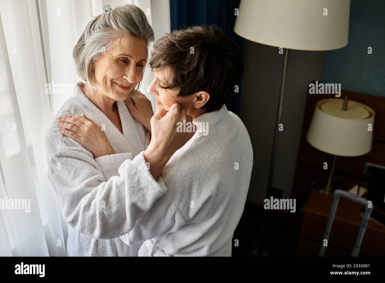 A senior lesbian couple in bathrobes sharing a tender embrace in a hotel. Stock Photo