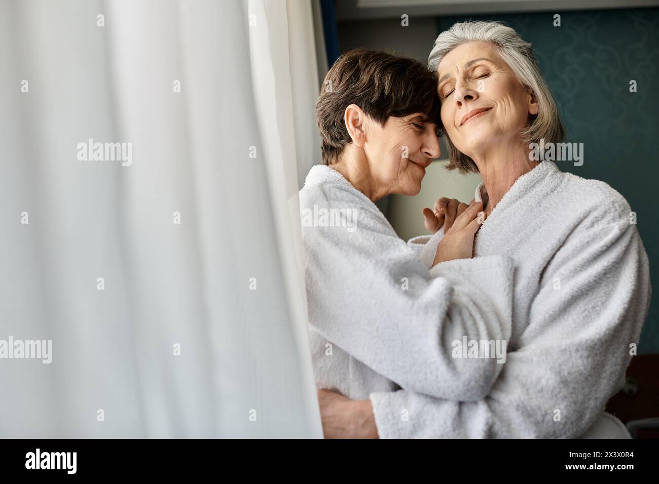 A senior lesbian couple, one in a bathrobe, hugging affectionately. Stock Photo
