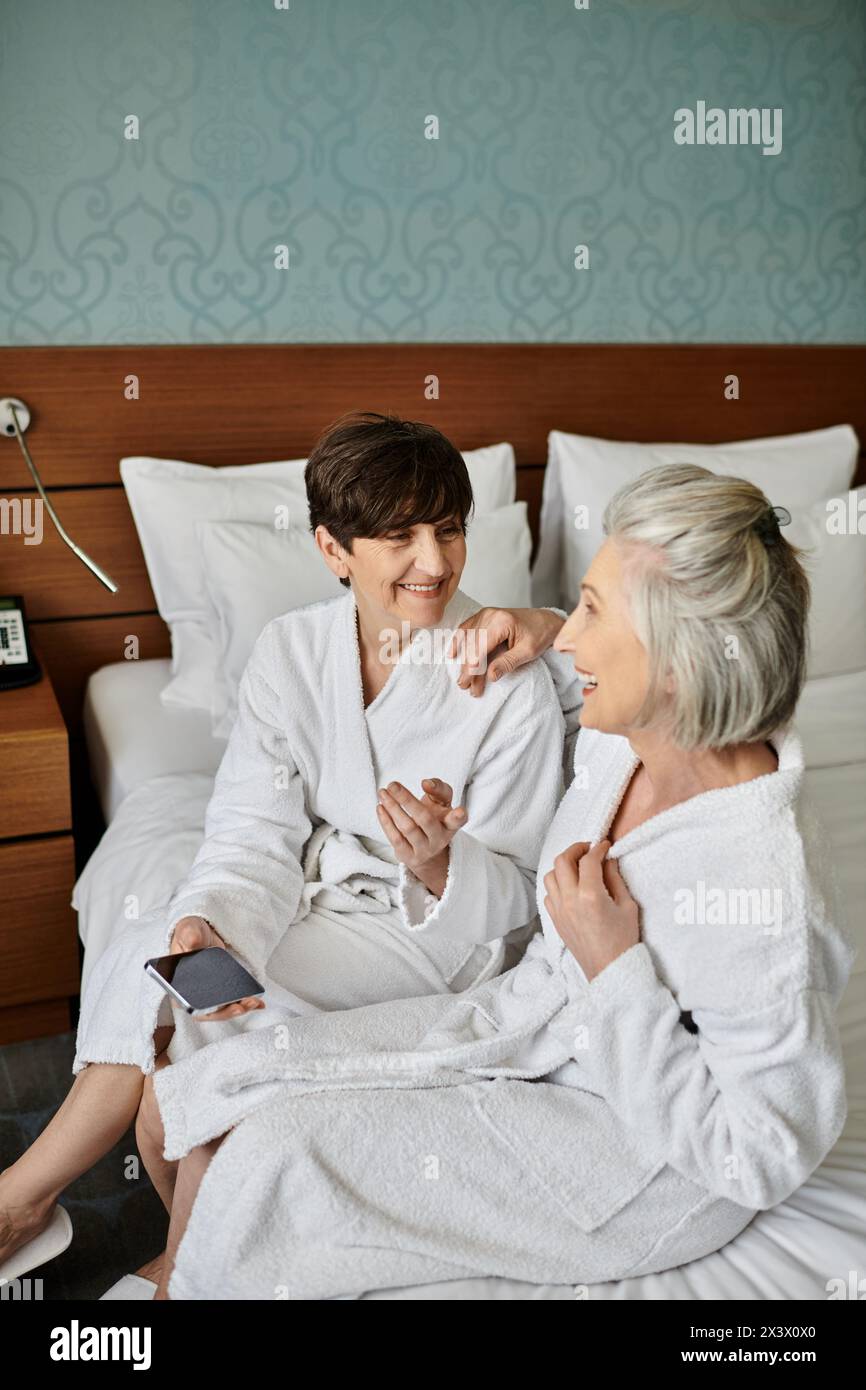 Senior lesbian couple on a bed in robes, sharing a tender moment. Stock Photo