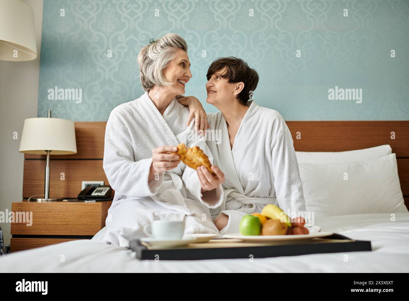Senior lesbian couple enjoying a tender moment on top of a cozy bed. Stock Photo