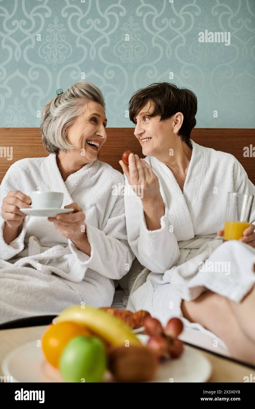 Two senior lesbian women sitting comfortably on a bed. Stock Photo