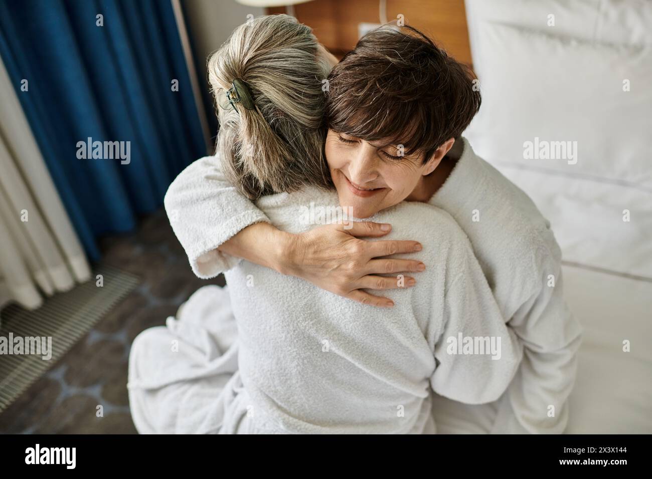 Senior lesbian couple sharing a tender hug in a hotel. Stock Photo