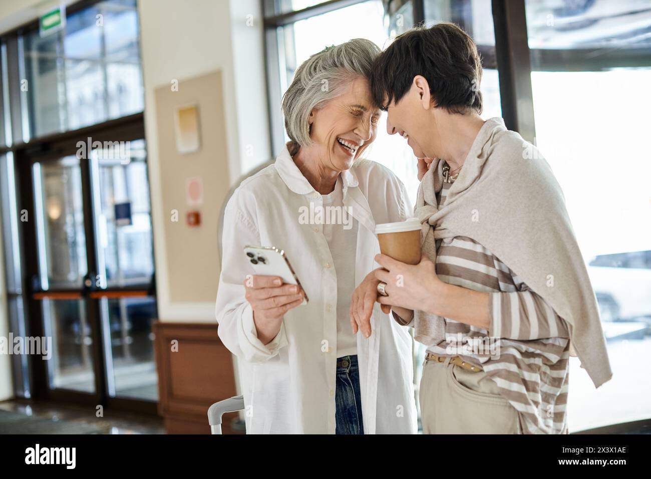 Two loving senior lesbian women standing in a hotel, embracing each other tenderly. Stock Photo