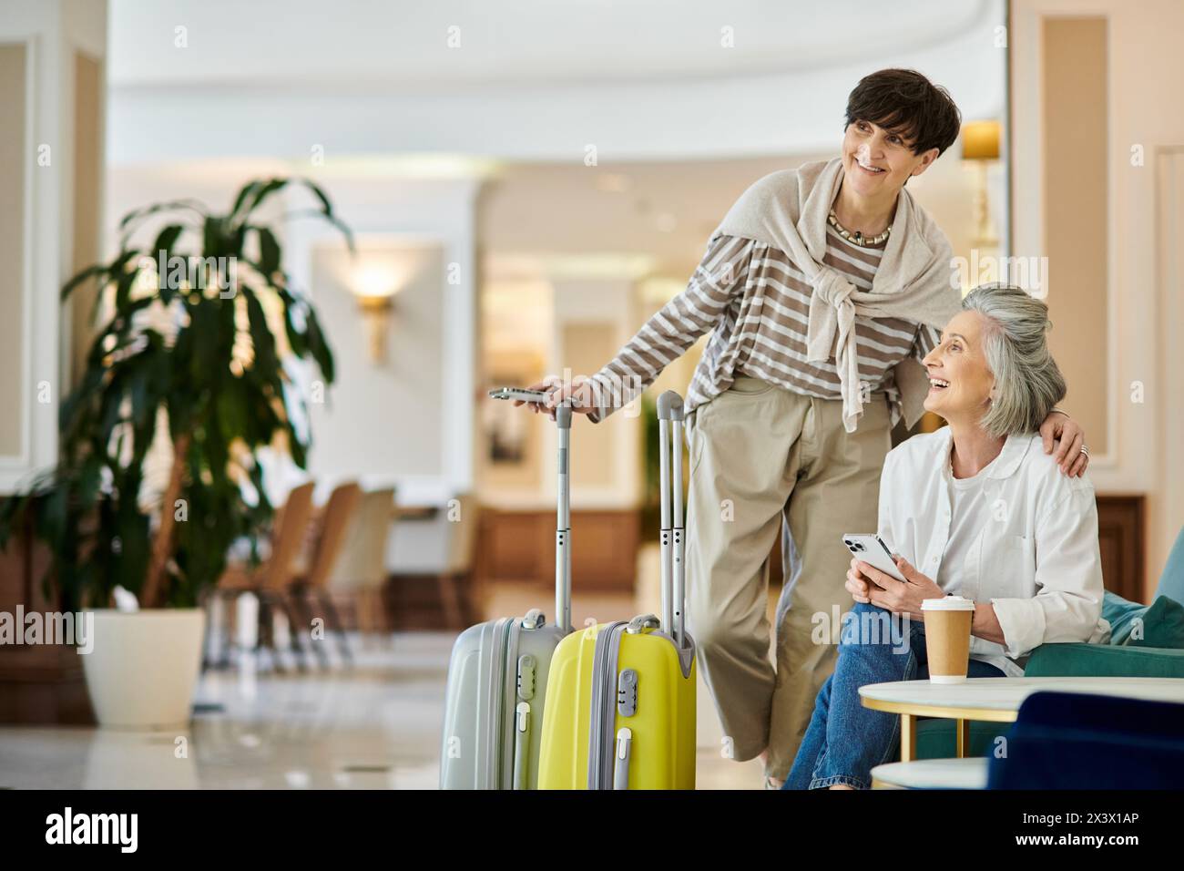 A senior lesbian couple, one standing, one with a suitcase, in a sweet moment. Stock Photo