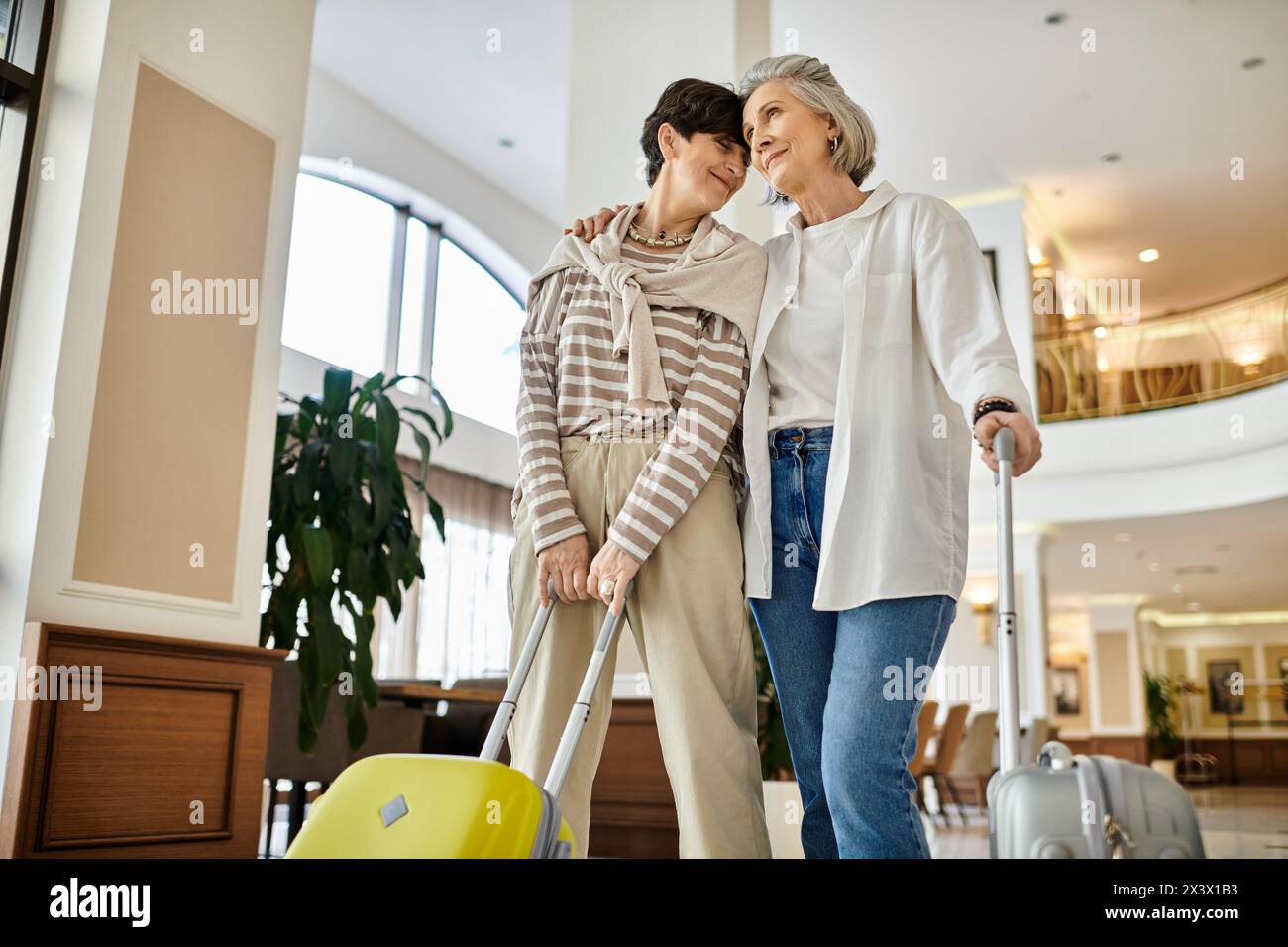 Senior lesbian couple, tenderly holding suitcases, ready for their journey. Stock Photo
