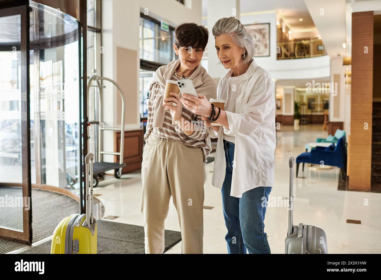Two women, a loving senior lesbian couple, standing in a lobby engrossed in a cell phone. Stock Photo