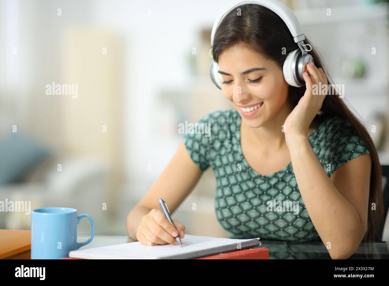 Happy student listening lesson with headphone and taking notes at home Stock Photo