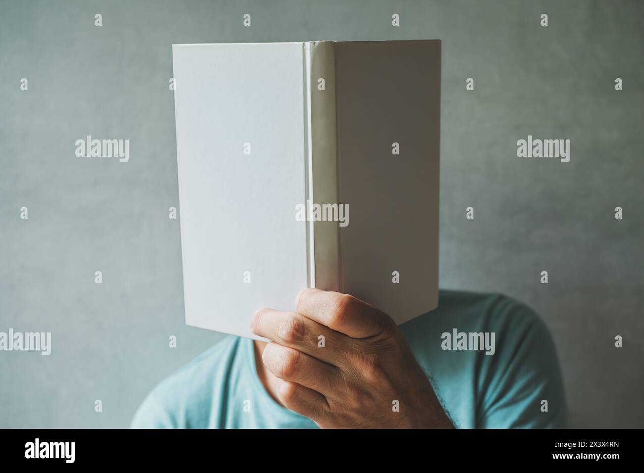 Male reader hiding his face behind the white mockup book, selective focus Stock Photo