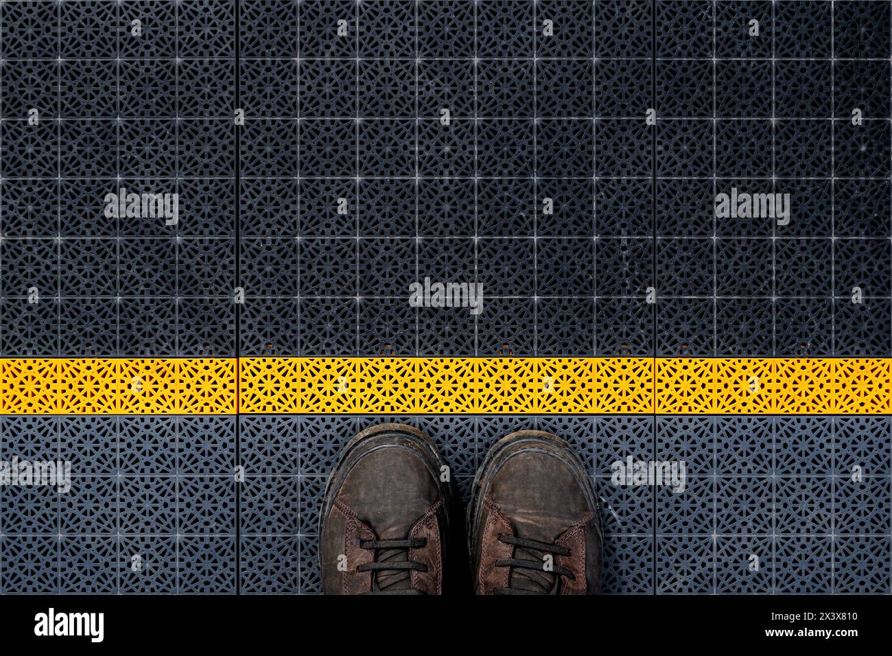Waiting line, male boots on non slip plastic flooring with triangular pattern from above, copy space included Stock Photo