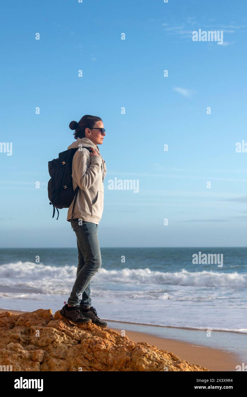 Woman hiker standing on a rock looking out to sea, getting away from it all. Stock Photo
