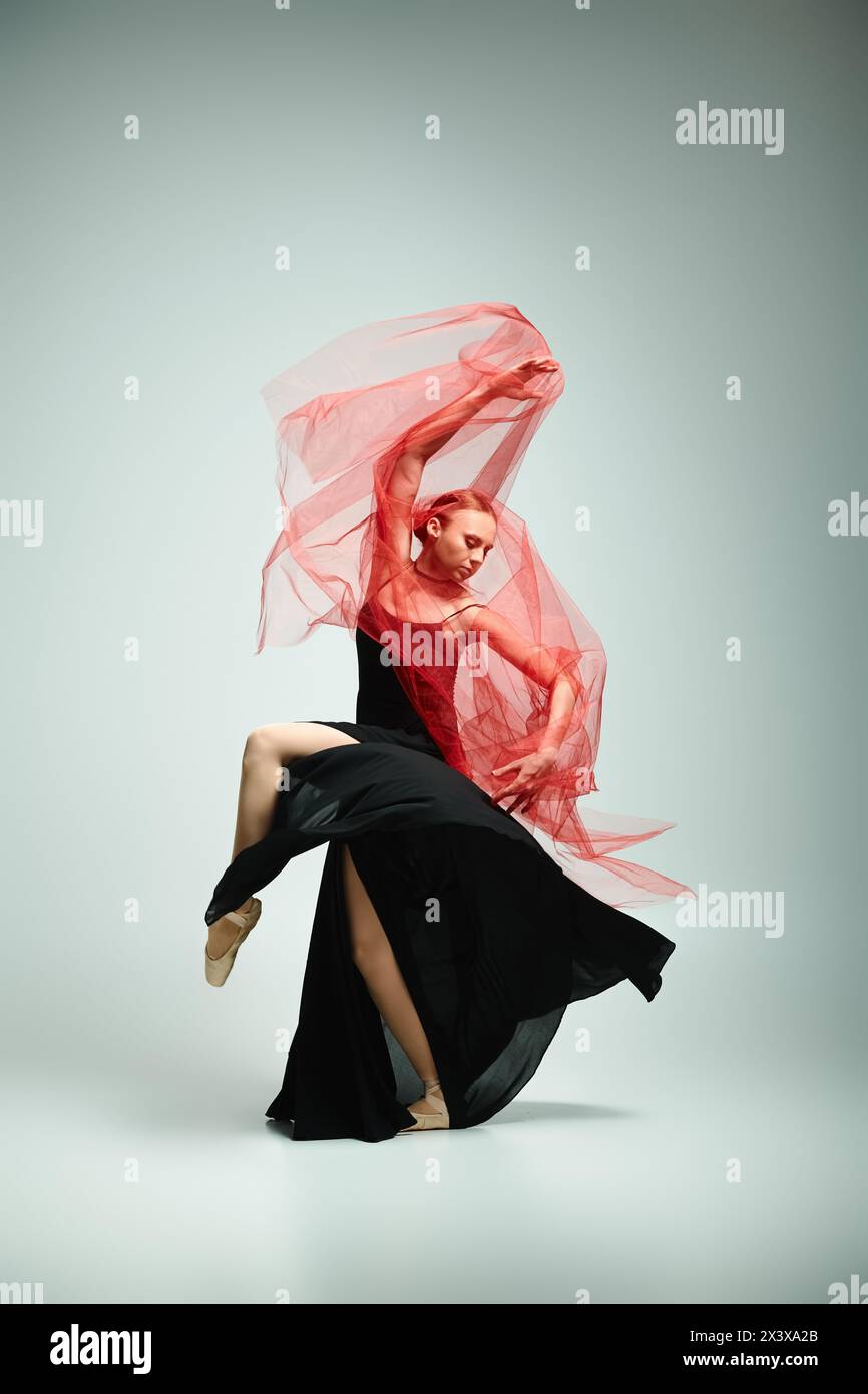 A young woman in a black dress and a red scarf gracefully dances. Stock Photo