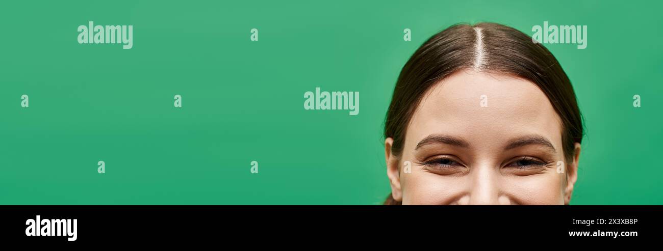 A young woman in her 20s smiles warmly against a vibrant green ...