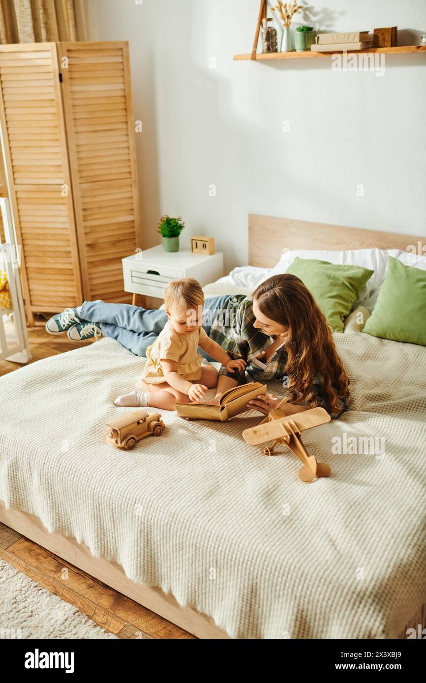 A young mother reading a book to her toddler daughter on a cozy bed ...