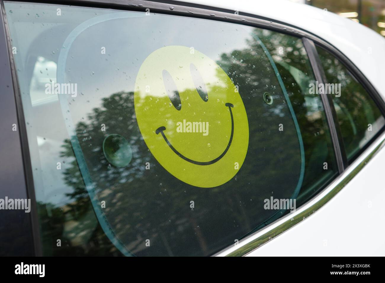 Yellow smiley face sunshade on back side window of white car Stock Photo