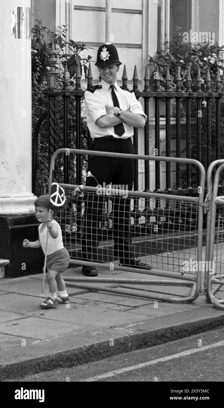 London, UK. 9th June 1984. A child plays with a small CND flag in front of a police officer during Grosvenor Square direct action blockade demonstration against Cruise missile deployment, London, UK. 9th June 1984  The non-violent, direct action protest  was in response to American President, Ronald Reagan's visit to the World Economic Summit in London and the deployment of US Cruise missiles in the UK.   The protest coincided with CND's anti Cruise missile rally in Trafalgar Square. London. Grosvenor Square was the location of the American Embassy in the UK at the time of the protest. Stock Photo