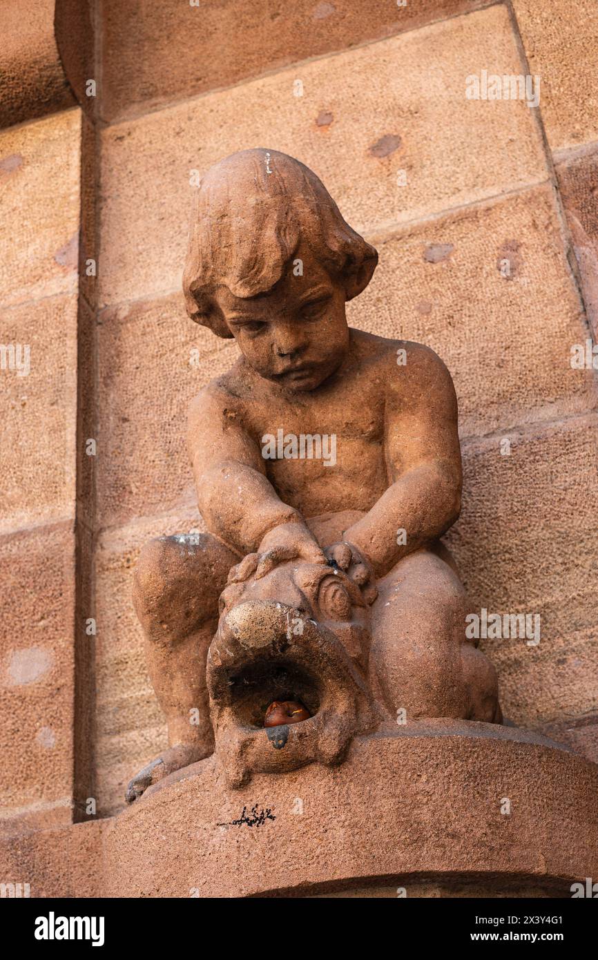 Rotten apple in the mouth of a fish, sculpture of a young boy on the exterior facade of the South Tyrol Museum of Archaeology, Bolzano, Italy. Stock Photo