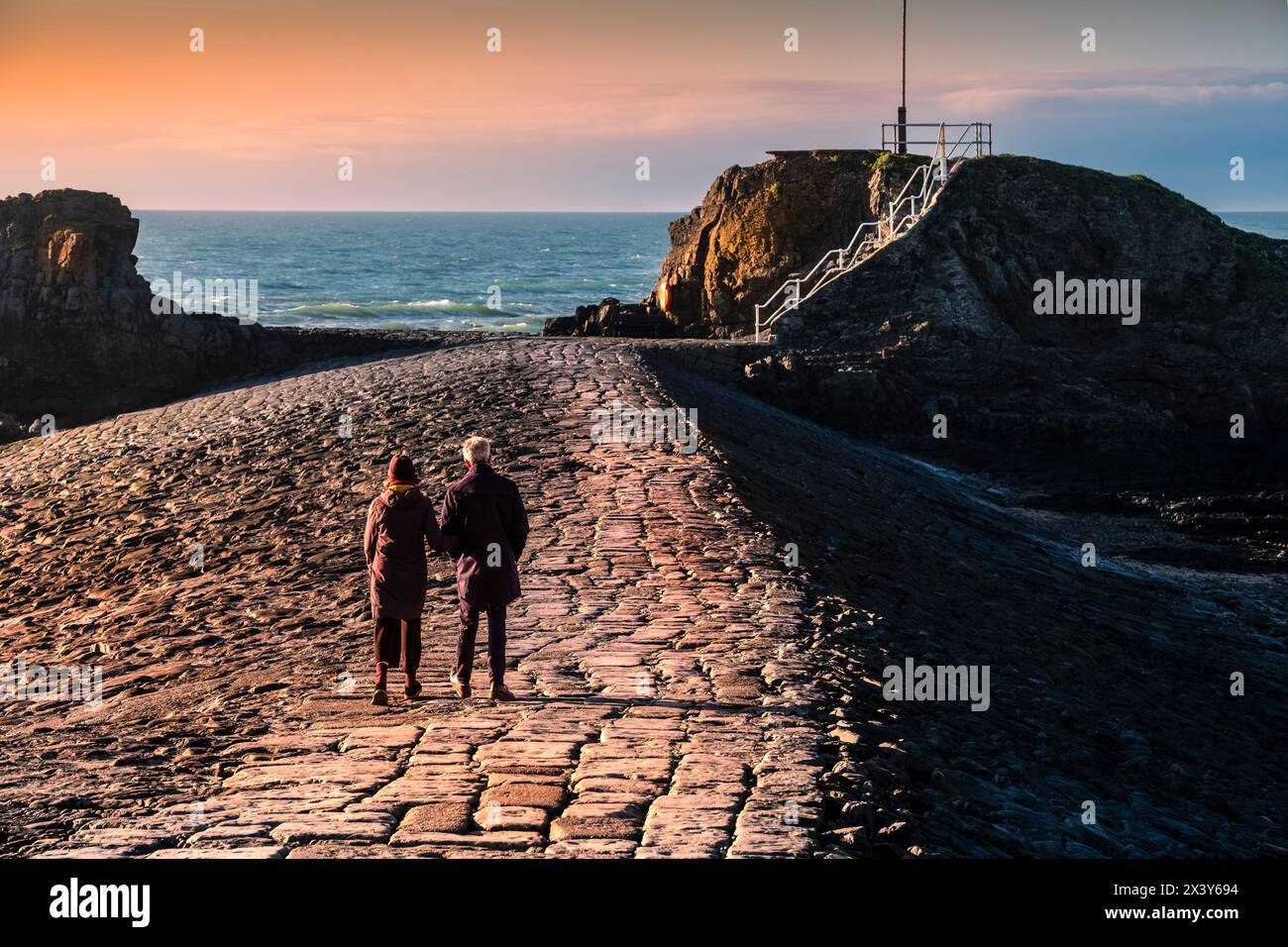 A mature couple walking along the breakwater levee in Bude in Cornwall in the UK. Stock Photo