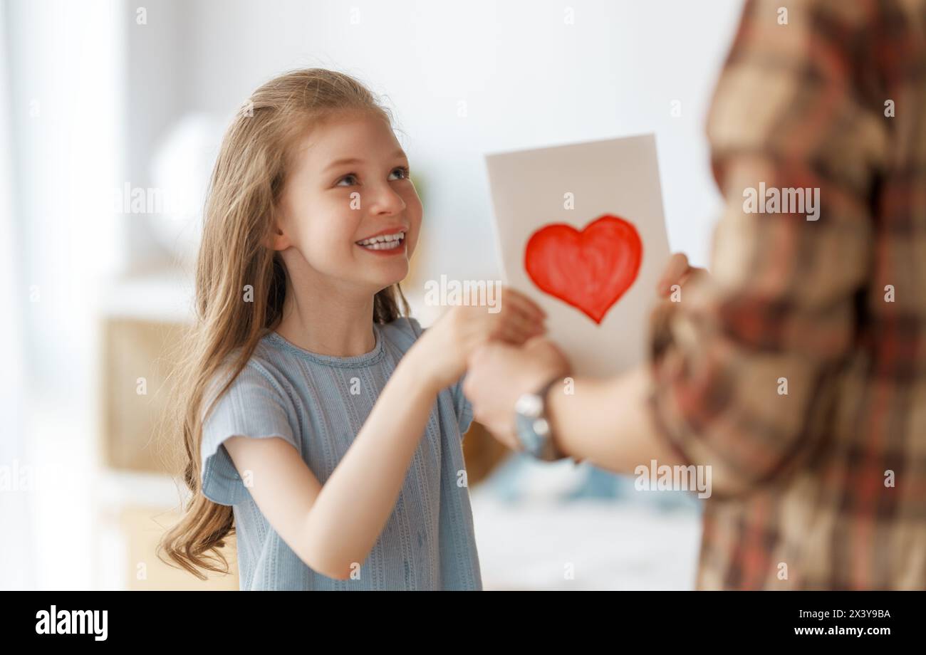 Child daughter is congratulating her father and giving him postcard. Girl is smiling. Family holiday and togetherness. Stock Photo