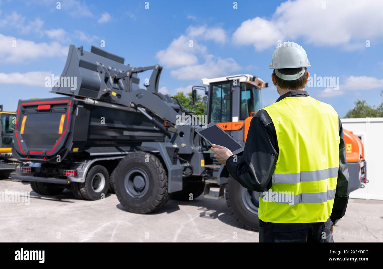 Engineer with a digital tablet on the background of construction machine. Stock Photo