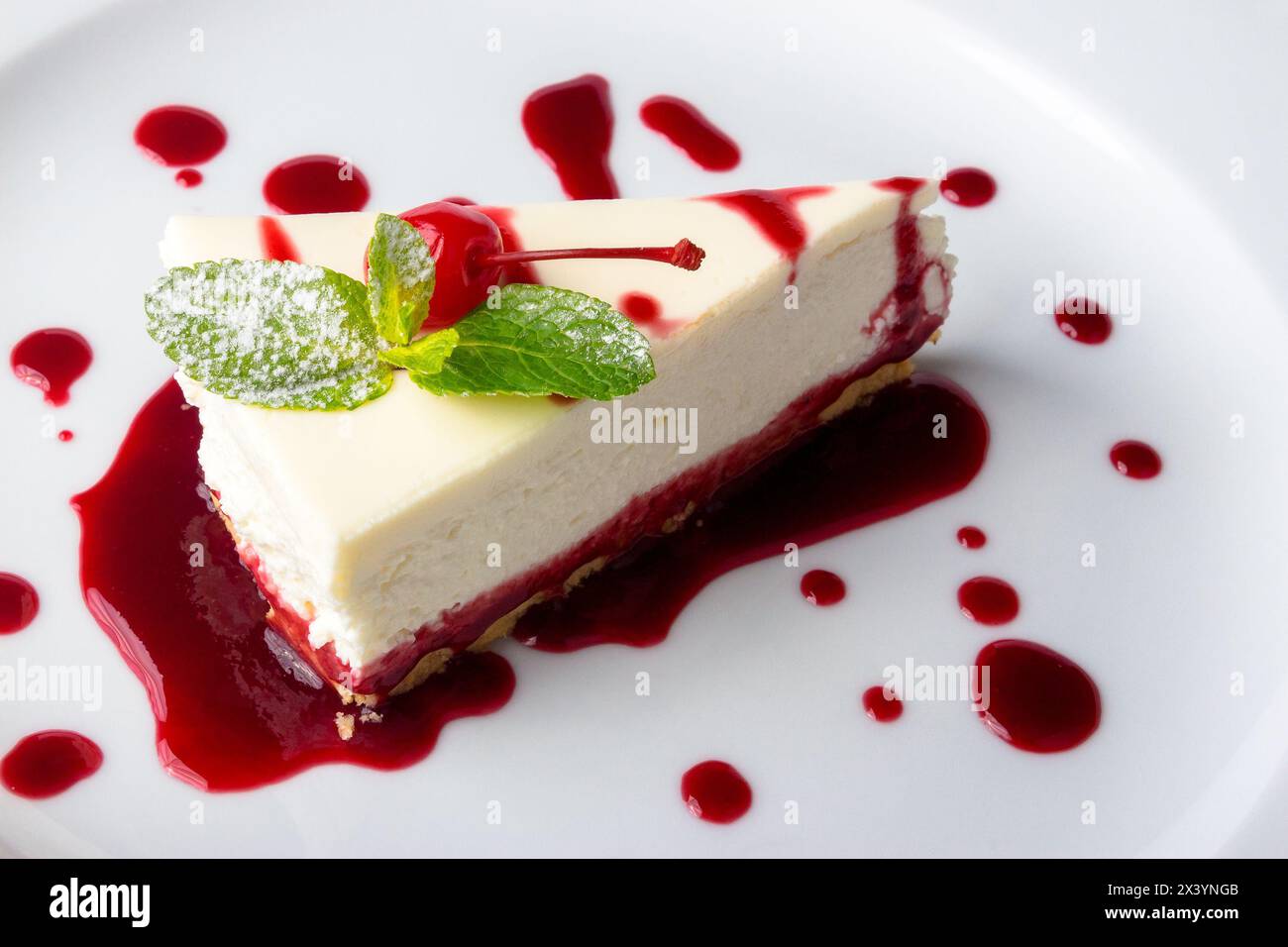 classic new york cheesecake in a raspberry syrup decorated with cherry and mint leaves Stock Photo