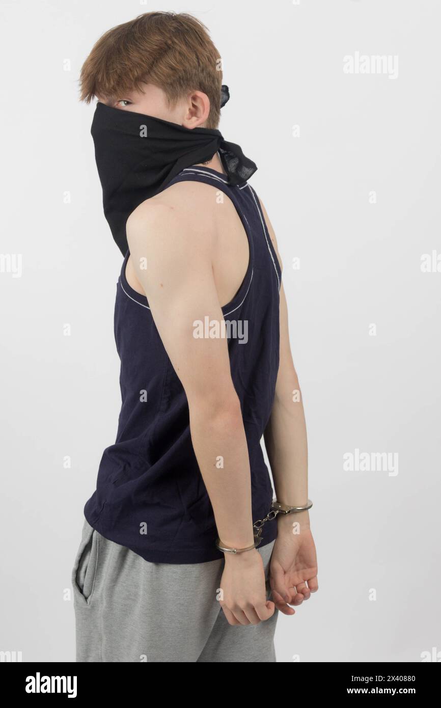 A Teenage Boy Wearing a Mask, Arrested in Handcuffs from Behind Stock Photo