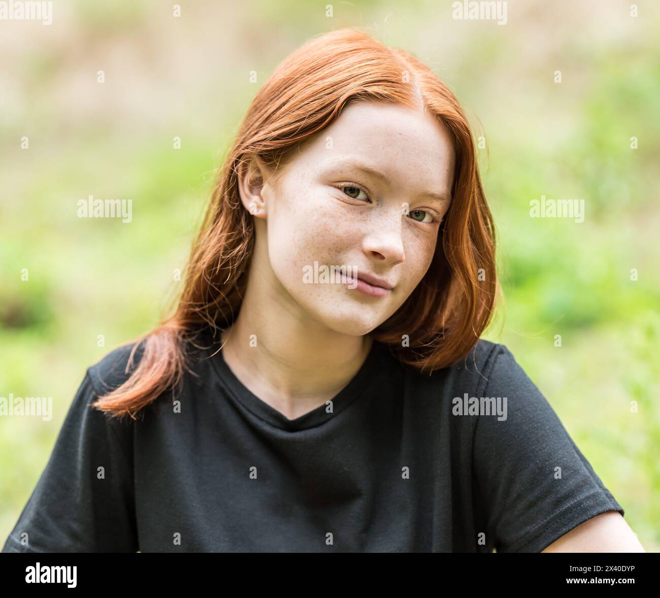 Red haired twelve year old girl with freckles posing with a nature bokeh background. Model released. Stock Photo