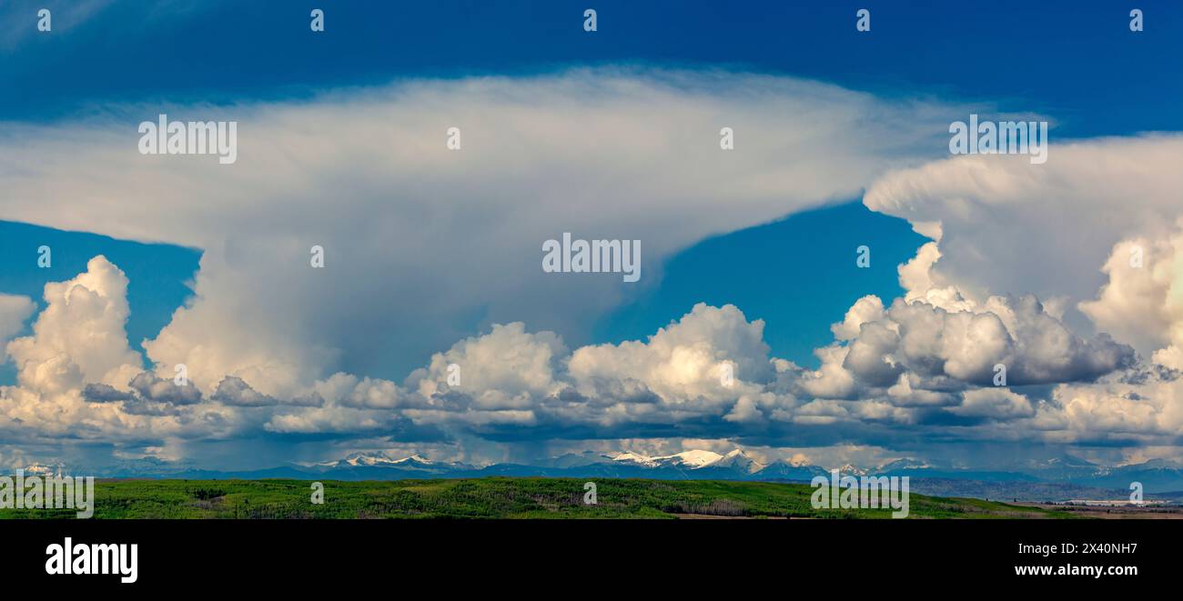 Panorama of storm clouds over the mountains and green foothills with blue sky, West of Calgary, Alberta; Alberta, Canada Stock Photo