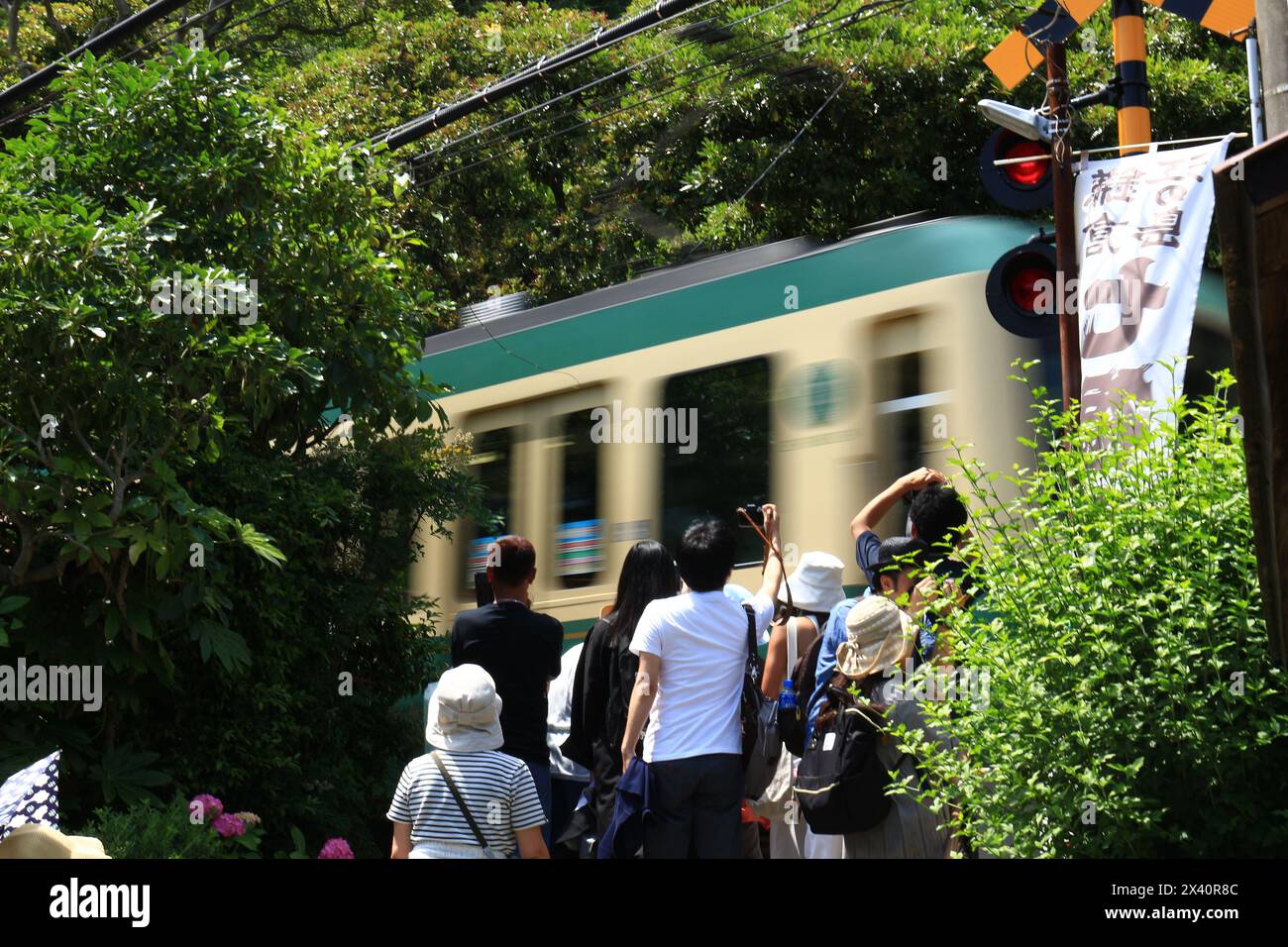 Daily life in Japan　People waiting for the train to pass and tourists taking pictures at the famous Enoden railroad crossing in Kamakura in summer Stock Photo