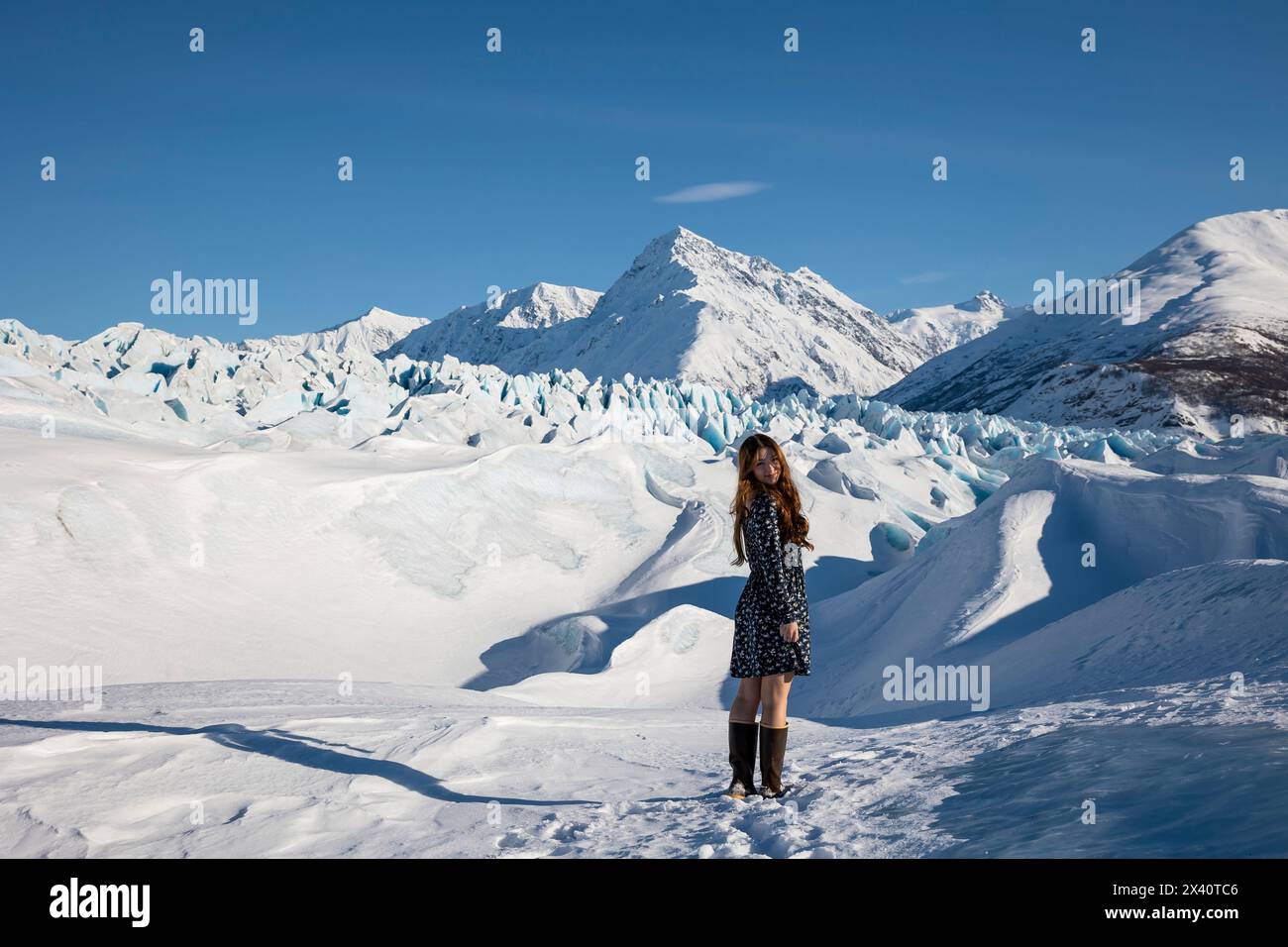 Teenage girl wearing a dress and boots standing on a glacier; Palmer, Alaska, Untied States of America Stock Photo