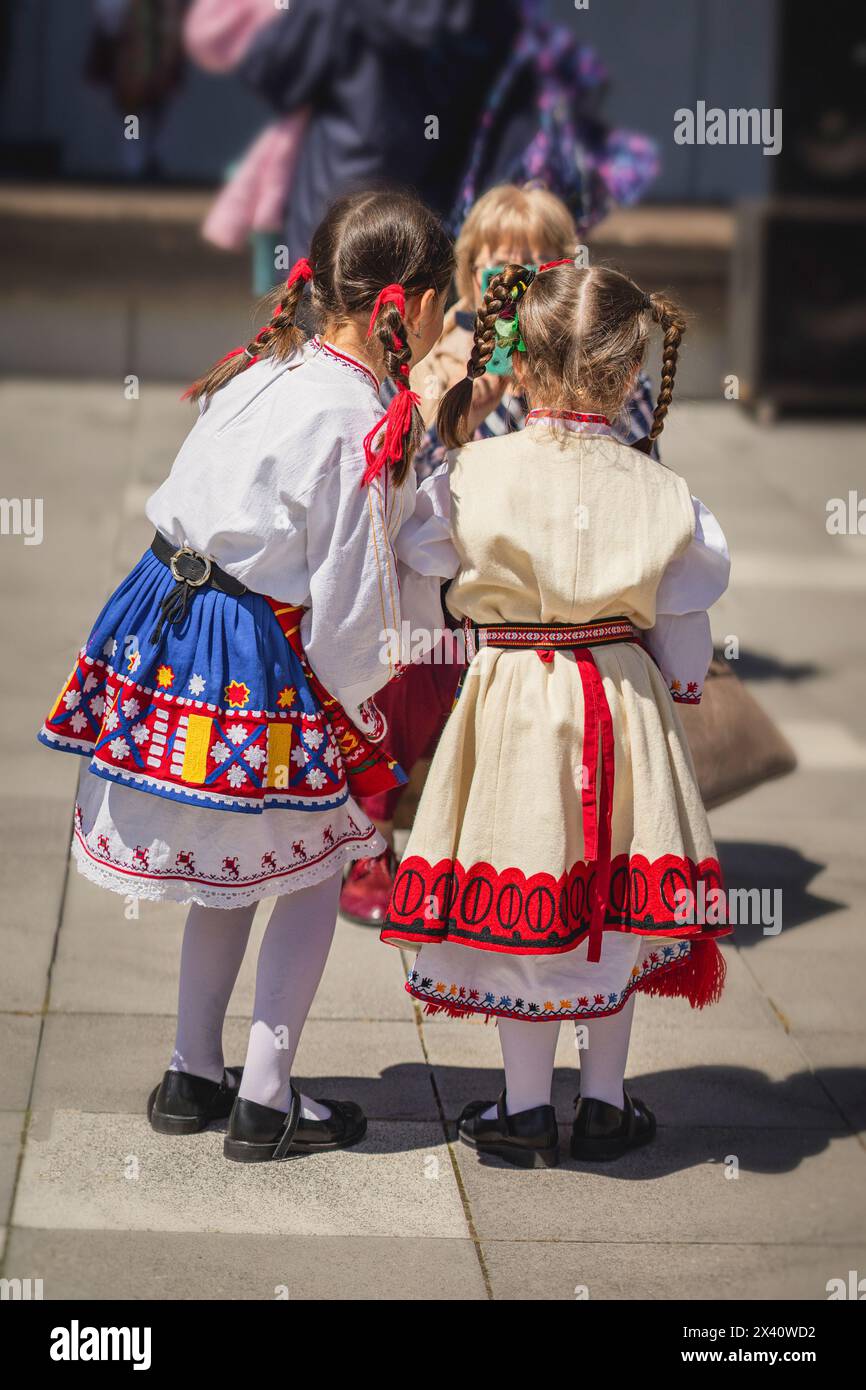 Two little girls in traditional national Bulgarian costumes at a folklore festival are photographed by their mother, rear view Stock Photo