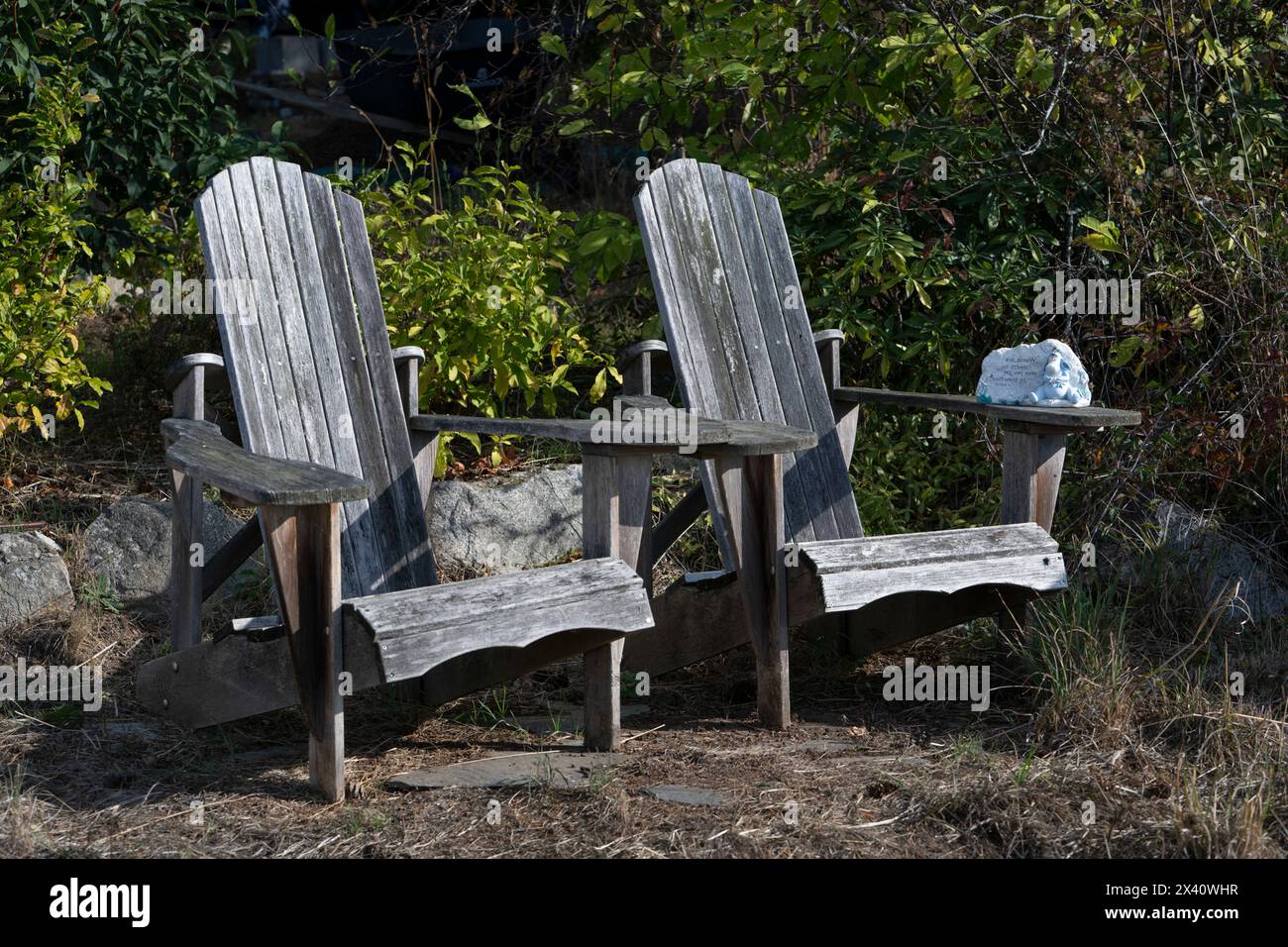Two weathered wooden Adirondack chairs side by side in the sunlight