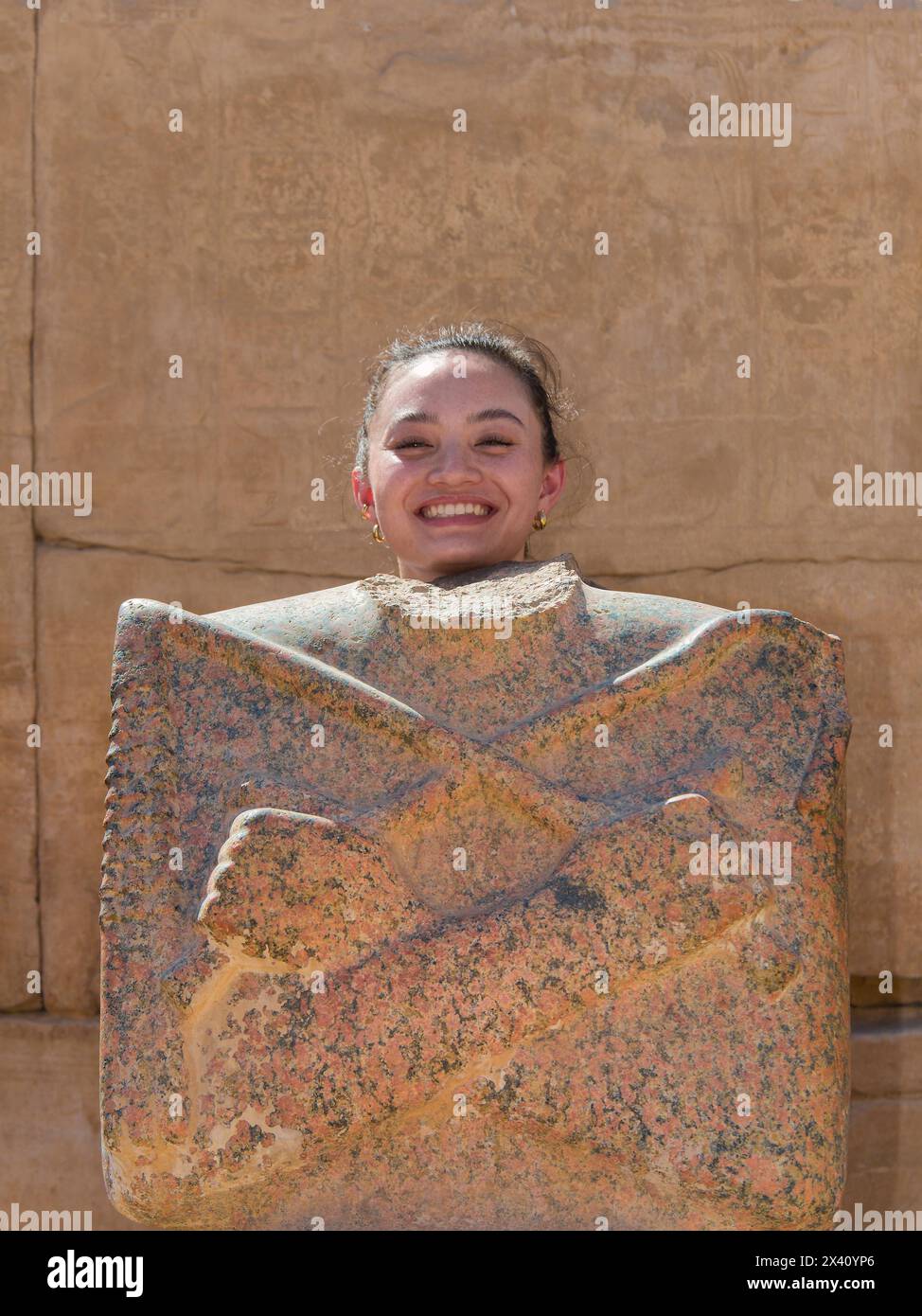 Girl posing as ancient Egyptian god with headless statue at the Karnak Temple in Luxor, Egypt; Luxor, Egypt Stock Photo