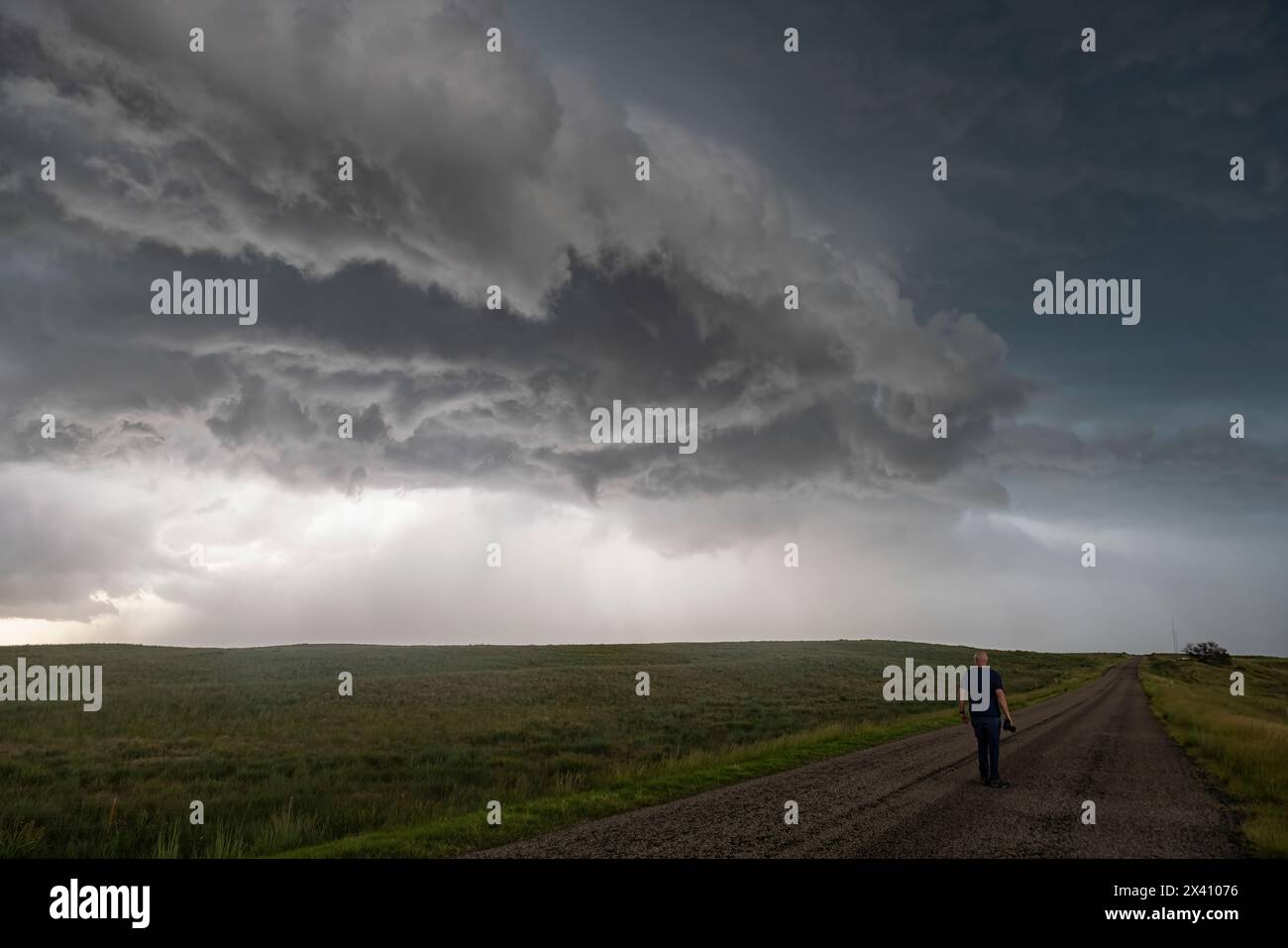Person walking  on a road while a huge thunderstorm is rolling across overhead. Stock Photo