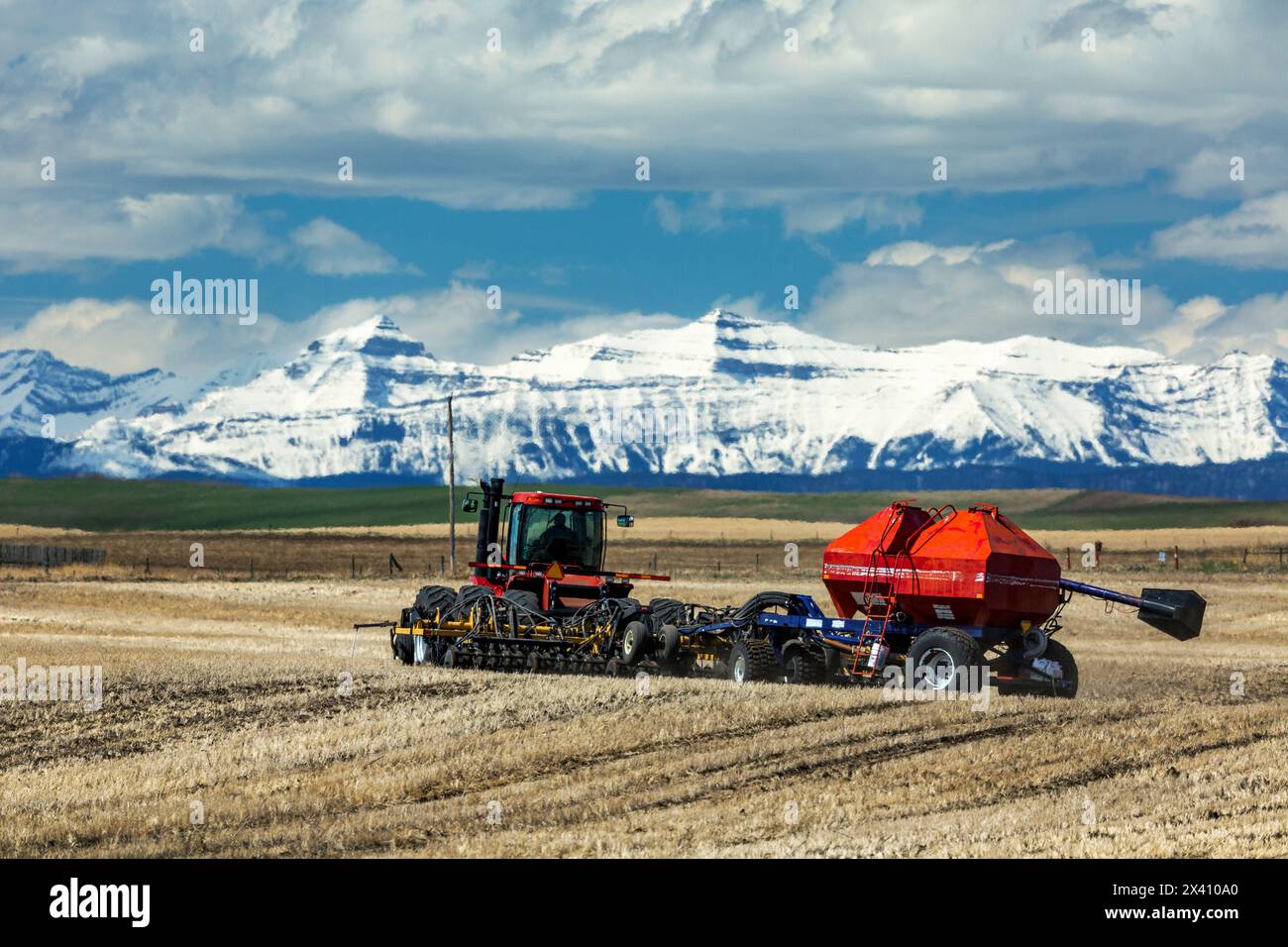 Tractor and seeder, seeding a field with snowcovered mountain range in