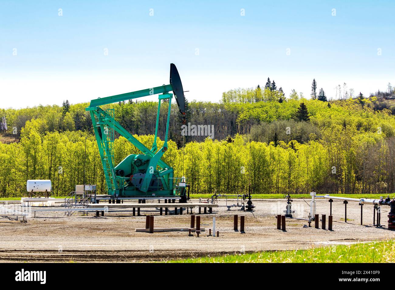 Pumpjack with pipelines and a treed hillside in the background; Longview, Alberta, Canada Stock Photo