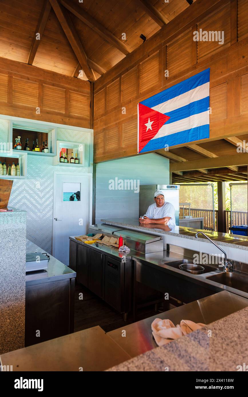 Tourist sits in a bar under a Cuban flag; Cayo Guillermo, Cuba Stock Photo