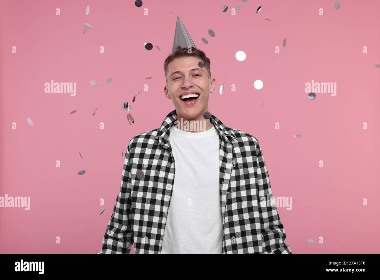 Happy man in party hat under falling confetti on pink background Stock Photo