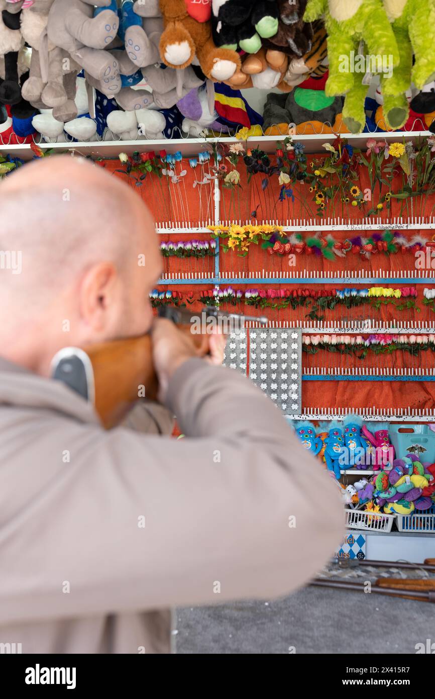 A rear view of a tourist playing shooting games to win plush toys on the wall at the fair. Shooting games. Stock Photo