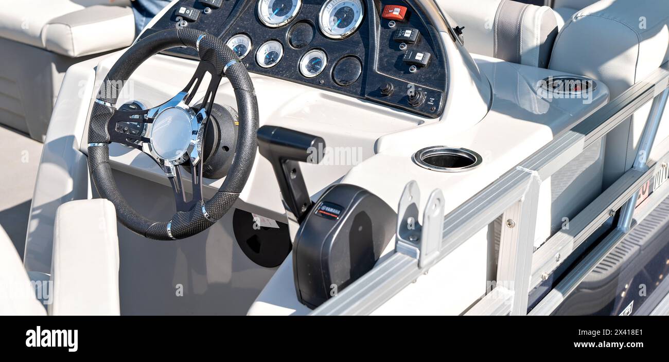 Pontoon boat cockpit dashboard and steering wheel being steered by the vessel captain as is moves slowly on a lake in Minnesota on a sunny summer day. Stock Photo