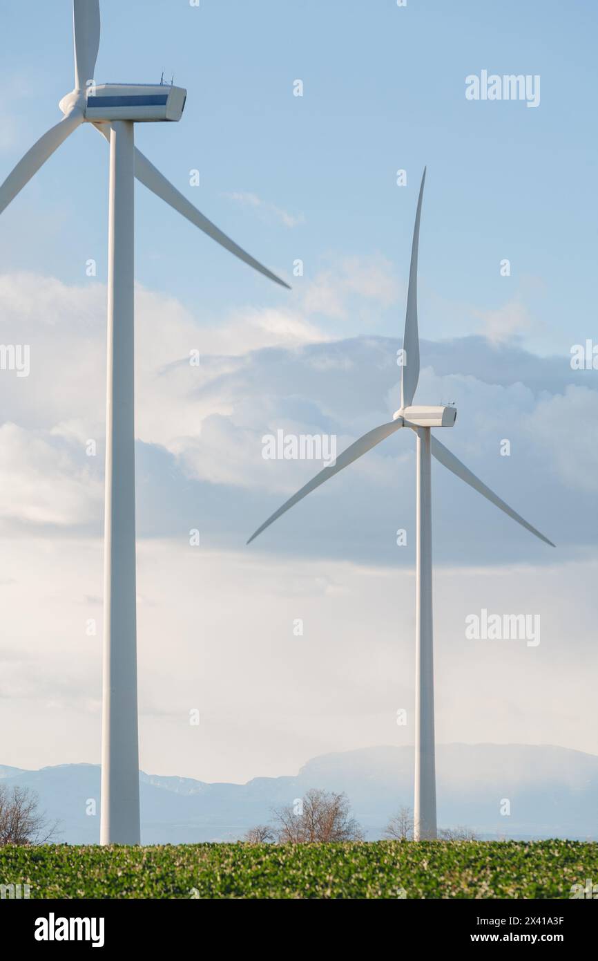 Two wind turbines are standing in a field with a cloudy sky in the ...