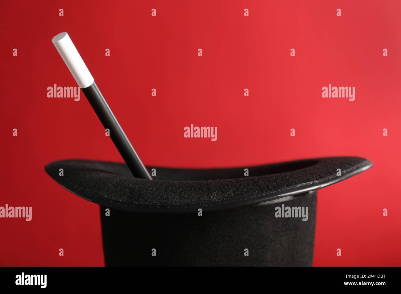 Black magician's hat and wand on red background, closeup Stock Photo