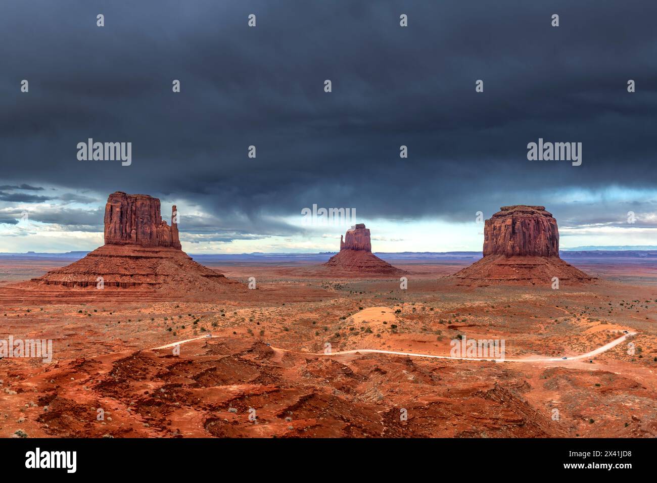 Storm clouds form over East, West and Merrick Butte at Monument Valley while sunshine still penetrates to highlight the vibrant red terrain and roadwa Stock Photo