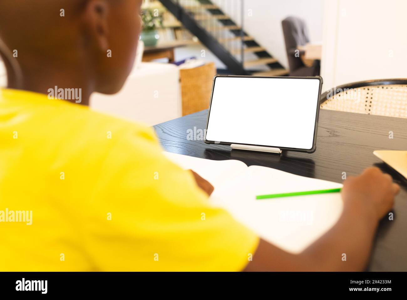 An African American boy in yellow shirt writing during video call at home, copy space Stock Photo