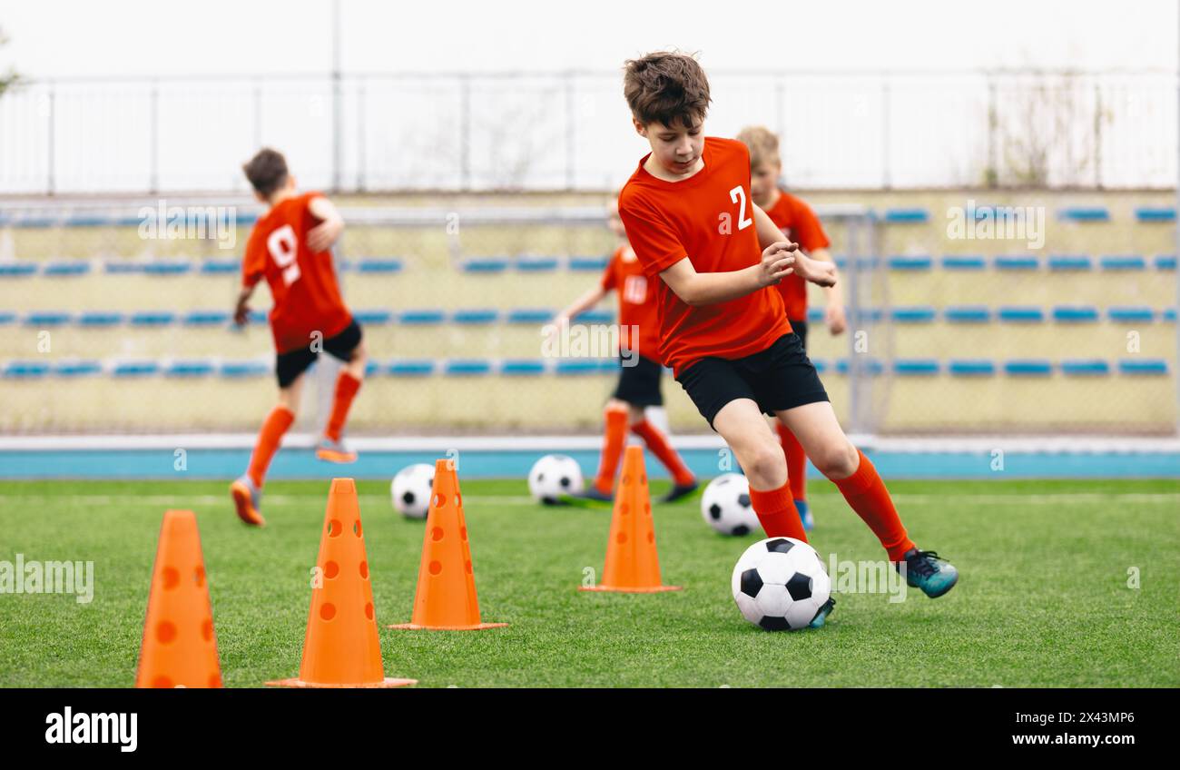 Happy Kids on Training Soccer Drill. Football Summer Camp. Young European Footballers Dribbling Around Cones in Drill. Soccer Boys in Red Uniforms in Stock Photo