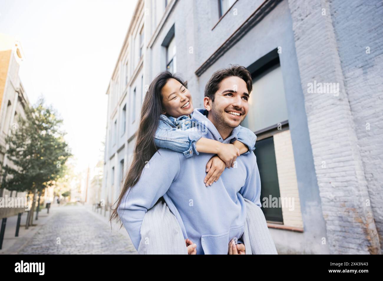 Young man carrying his girlfriend on his back walking on the city street. Couple piggybacking on city street. Stock Photo